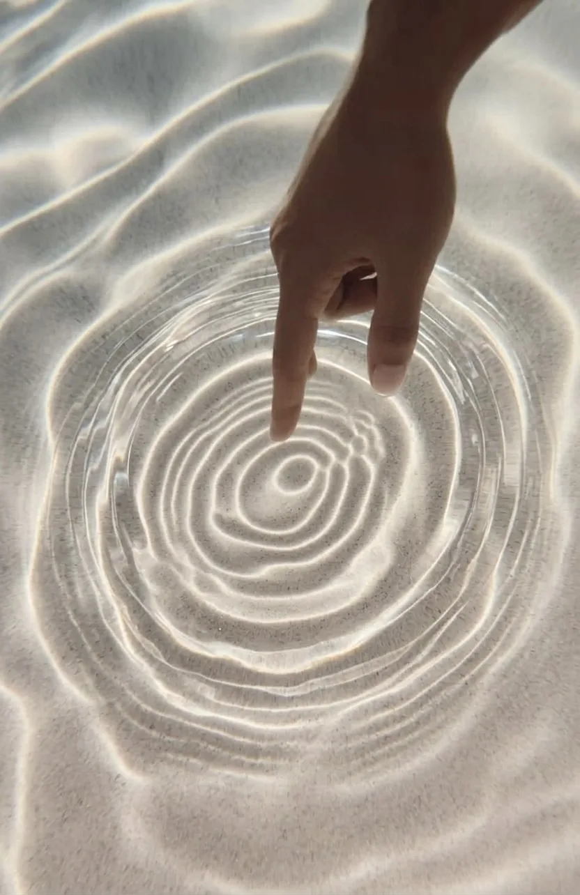 A fingertip touching still water, sending out concentric ripples over sand — clarity from a single point.