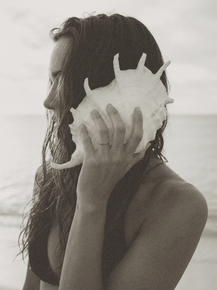 A woman on the beach holding a conch shell to her ear