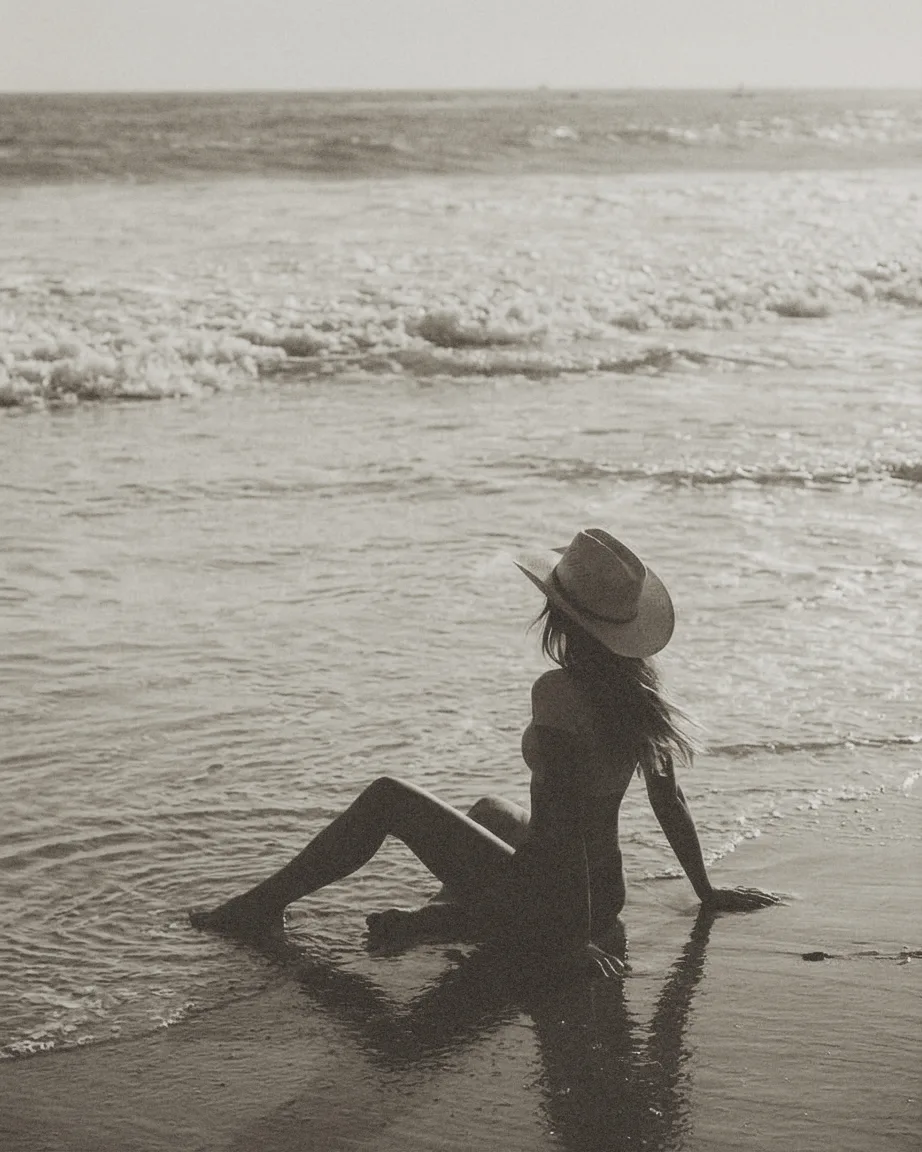 Woman in a straw hat sitting at the water's edge at golden hour